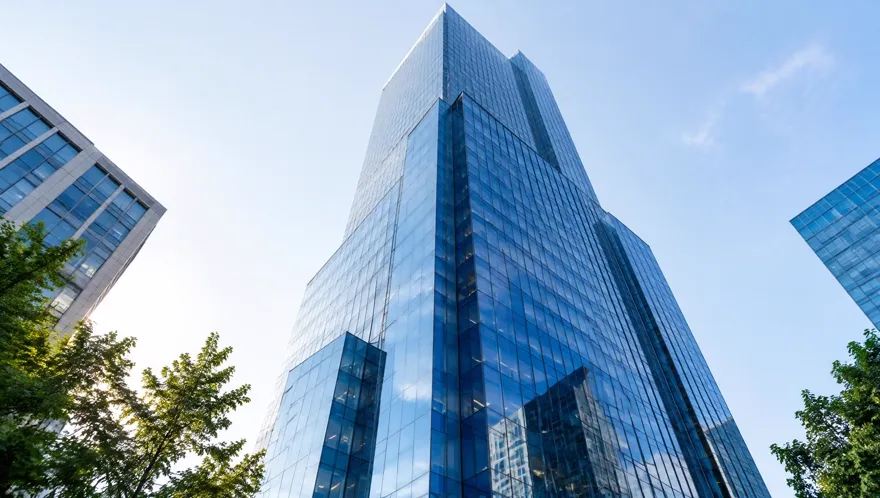 Low-angle view looking up at a tall modern glass office tower in bright morning light