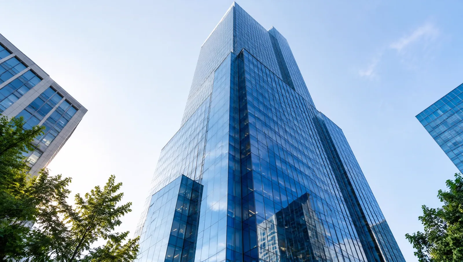 Low-angle view looking up at a tall modern glass office tower in bright morning light