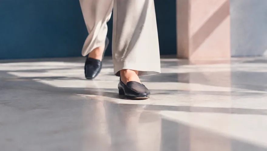 Close-up of feet walking across a sunlit polished floor beside a deep blue wall