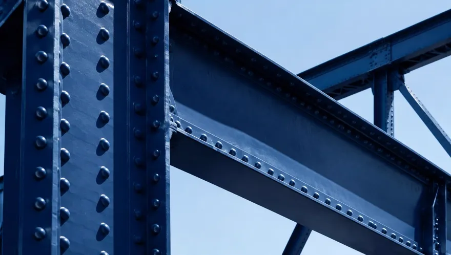Close-up of deep blue steel bridge girders and rivets against a bright sky